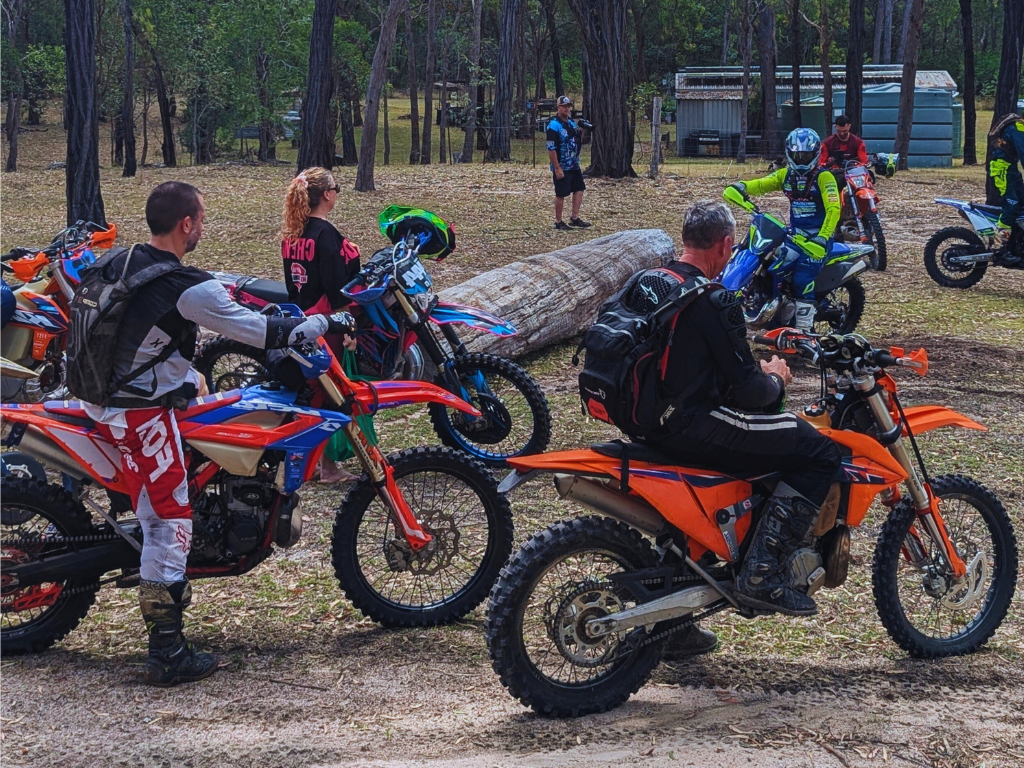 Motorbike riders racing on a dirt track, kicking up dust as they compete.