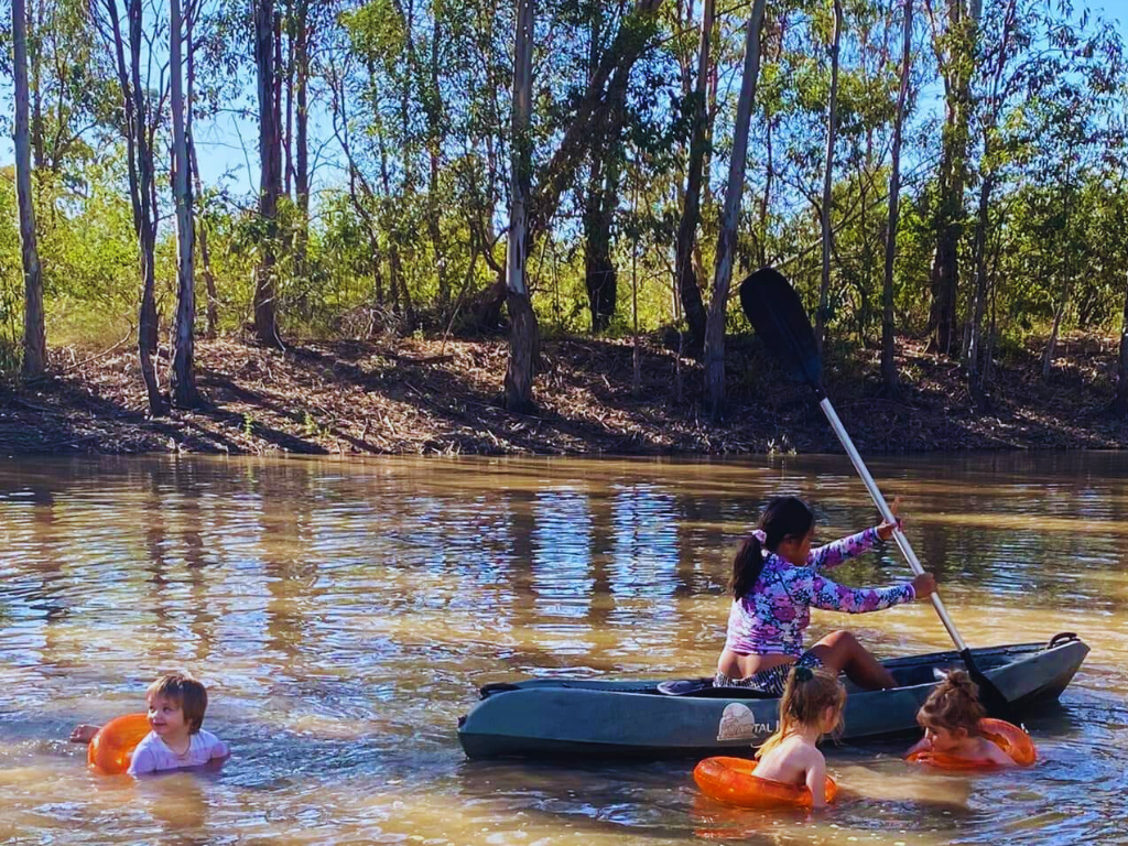 A serene campsite in Childers, surrounded by tall trees and open fields and campers enjoying the place.